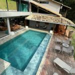 Casa de campo com piscina retangular, deck, espreguiçadeiras e área coberta ao redor.